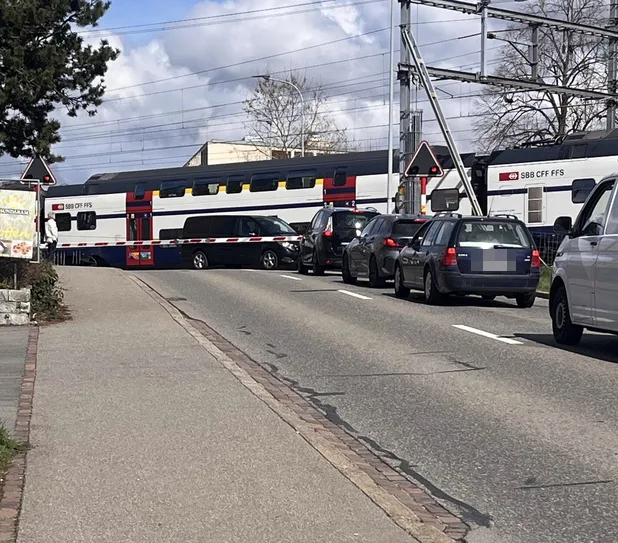 Ein Auto steht hinter der Barriere, während ein Zug durchfährt.